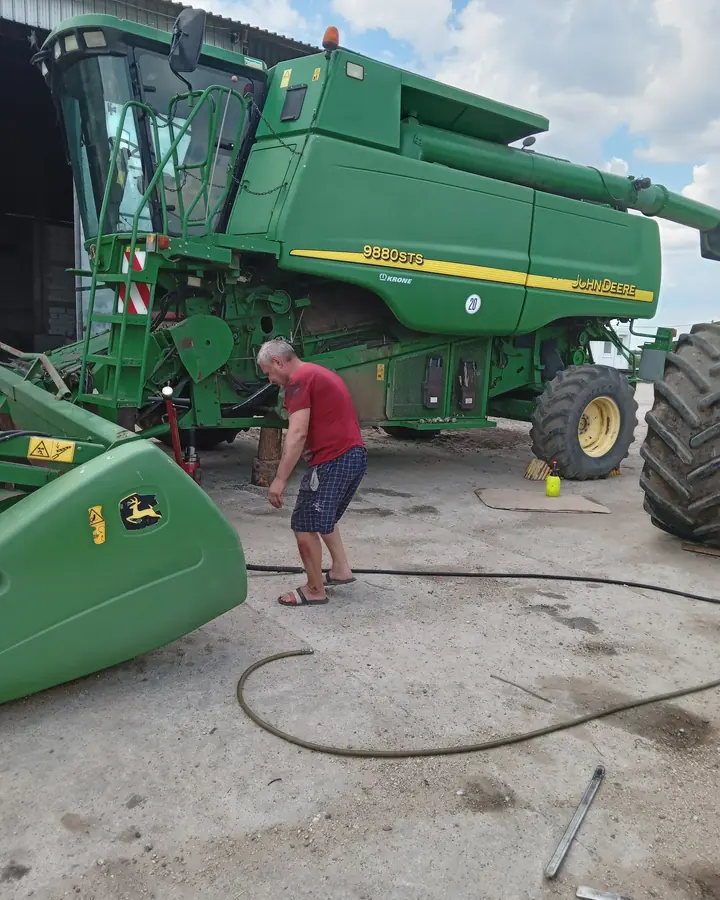 Mecanic la roata unei combine John Deere, cu cricul sub utilaj