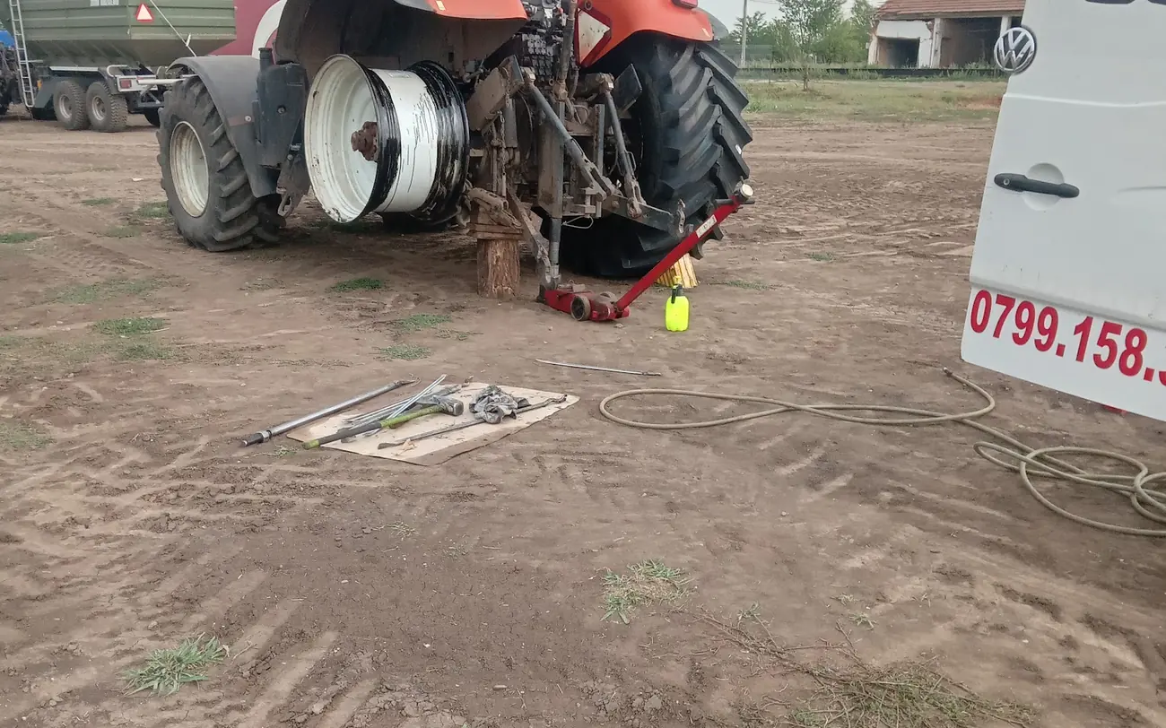 Tractor cu roata din spate demontată pe teren, lângă duba de vulcanizare mobilă