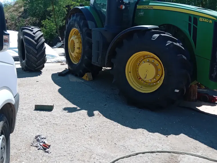Tractor John Deere cu roata din spate demontată, în curtea unei ferme