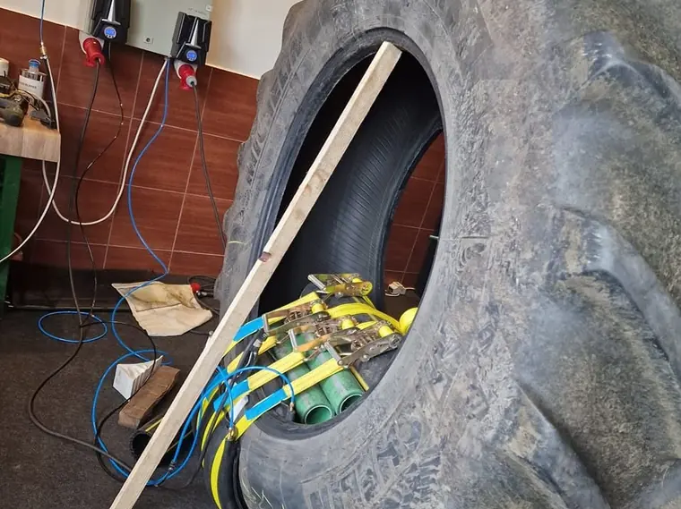 Anvelopă mare de tractor prinsă cu chingi în presa de vulcanizare, în atelier