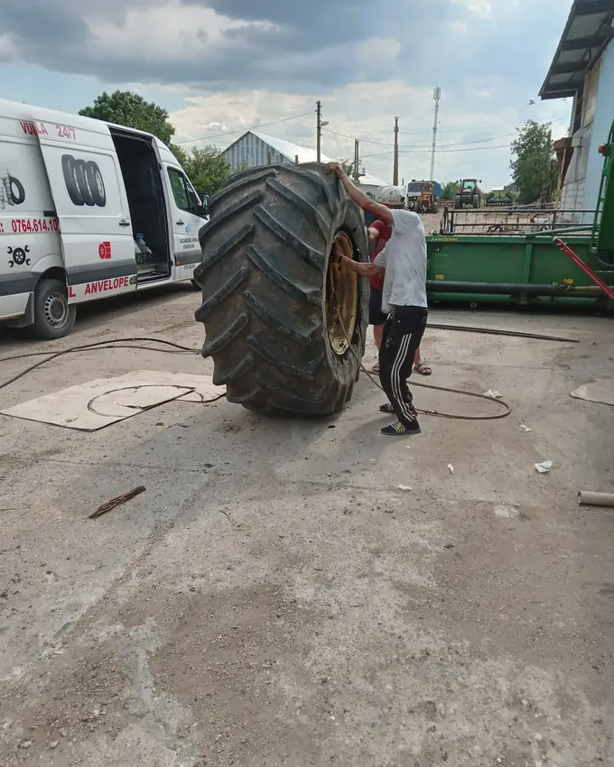 Roată mare de tractor ținută în picioare lângă duba de vulcanizare